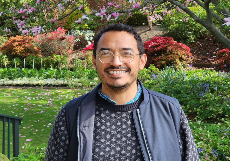 Man in a blue jacket ,patterned jumper and glasses standing in a park