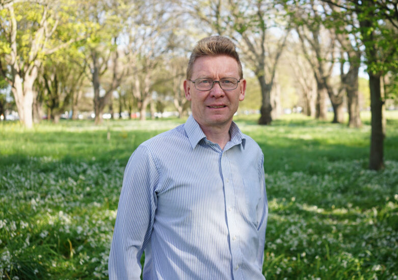 Man in light coloured shirt standing in a park on a sunny day
