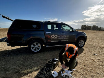 Man with drone equipment crouching in front of a truck on a sunny day