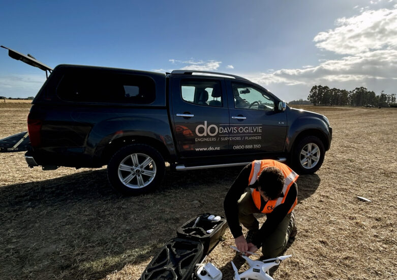 Man with drone equipment crouching in front of a truck on a sunny day