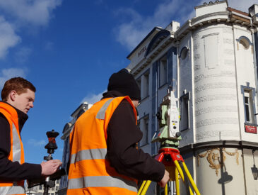 Two men with hi-vis with survey equipment on a sunny day