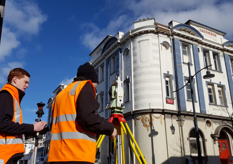 Two men with hi-vis with survey equipment on a sunny day