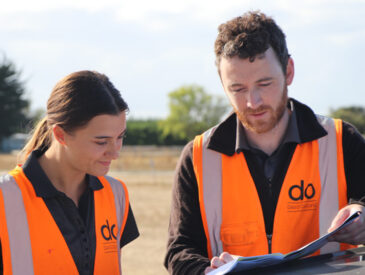 Man and woman dressed in high visibility vests looking at paper documents