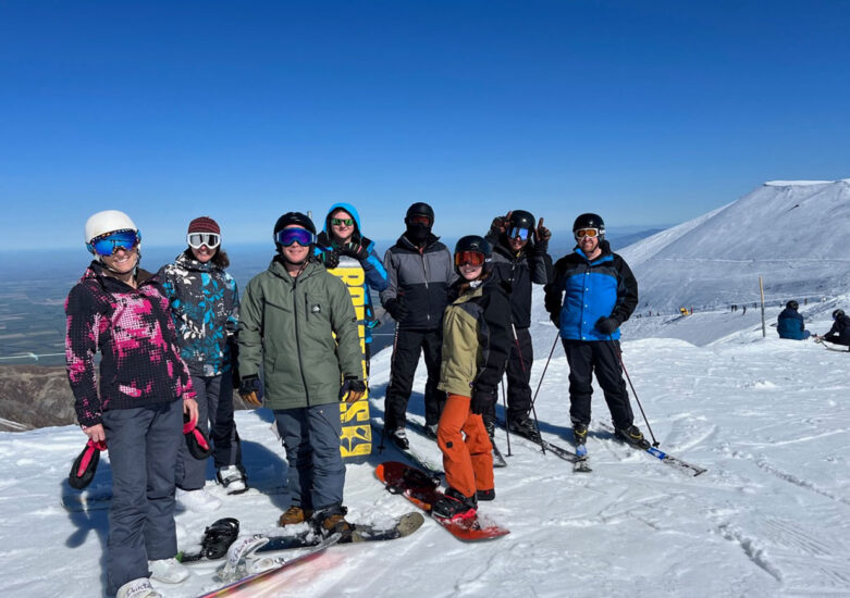 Group of people dressed in ski clothing standing on a snowy mountain on a blue sky day